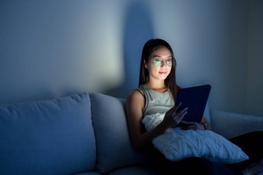 Gözlüklü ve evdeki tablet bilgisayardan izleyen bir kadın.