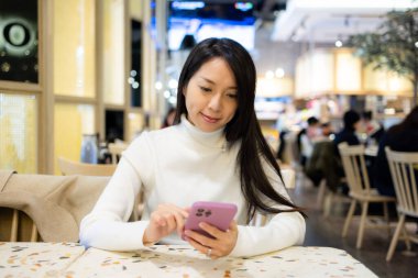 Kadın restoranda cep telefonu kullanıyor.