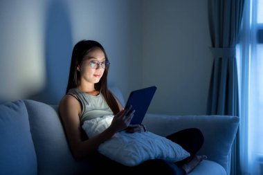 Gözlüklü ve evdeki tablet bilgisayardan izleyen bir kadın.