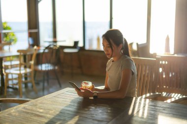 Kahve dükkanında gün ışığı altında cep telefonu kullanan kadın.