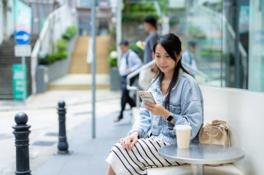 Kadın kafenin önünde telefonuyla oturuyor.