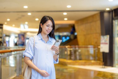 Alışveriş merkezinde Asyalı hamile kadın cep telefonu kullanıyor