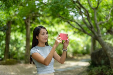 Kadın parkta fotoğraf çekmek için cep telefonu kullanıyor.