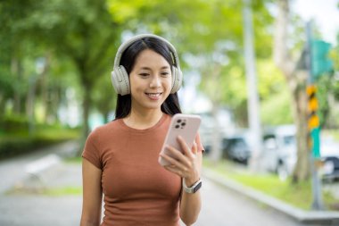 Kadın kulaklık takıyor ve sokakta akıllı telefon kullanıyor.