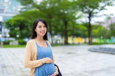 Hamile kadın parktaki kameraya gülümsüyor.