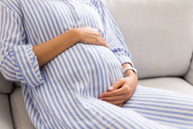 Hamile kadın karnını tutar ve evdeki kanepeye oturur.