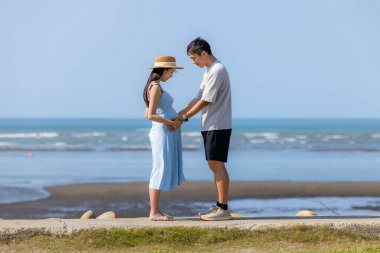 Asyalı çift deniz kenarındaki hamile karnına bakıyor.