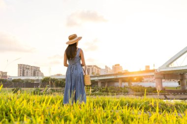 Mavi elbiseli bir turist ve nehir kenarındaki parkın gün batımının tadını çıkarıyor.