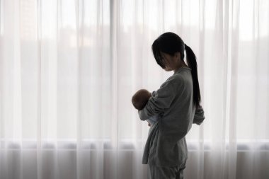 Anne bebeğini kucağına al ve perdenin yanında dur.