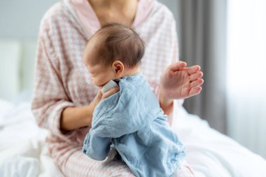 Anne geğirerek bebeği rahatlatıyor ve yatağa oturuyor.