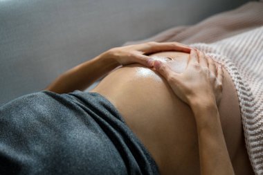 Asyalı hamile kadın göbeğine yağ sür.