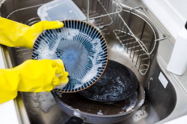 Kadın mutfak lavabosunda bulaşık yıkıyor.