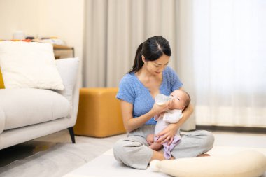 Asyalı anne evde bir şişe süt besliyor.