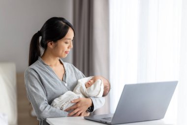 Annem dizüstü bilgisayarla uğraşırken yeni doğan bebeğe bakıyor.
