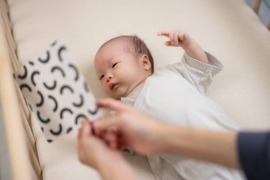 Yeni doğmuş bebek, yatağın üzerindeki siyah beyaz kontrast kartına bak.