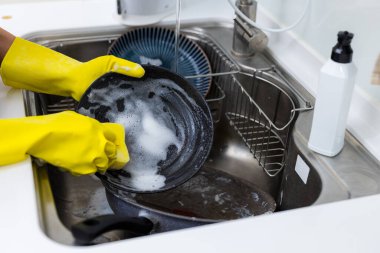 Kadın mutfak lavabosunda bulaşık yıkıyor.