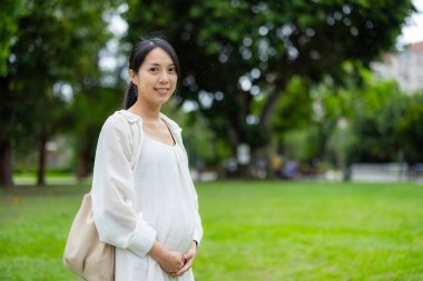 Yeşil park ortamında dinlenen hamile bir kadın.