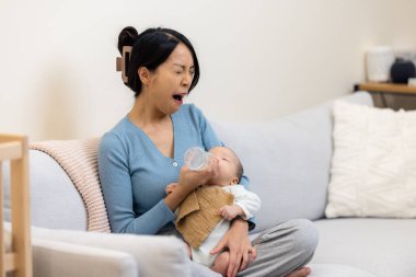 Anne bebeği beslerken esniyor.