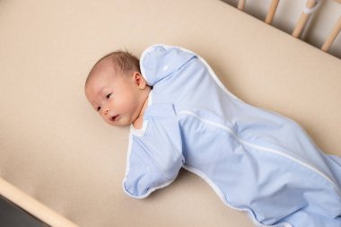 Asyalı yeni doğmuş bebek kundak takar ve bebek beşiğinde yatar.