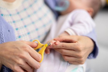 Bakıcı anne makas kullanarak bebek tırnaklarını kesiyor.