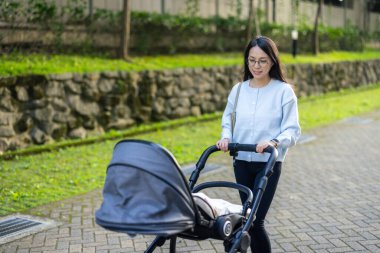 Anne açık alanda bebek arabasında bebeğe bakıyor.