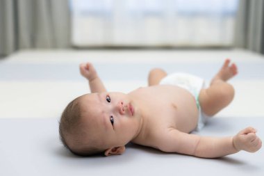Sevimli bebek yumuşak oyun minderinde uzanmış bez beziyle