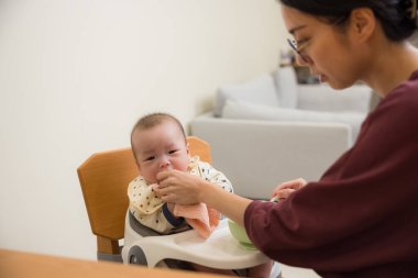 Anne evde kaşıkla bebeği besliyor.