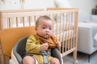 Bebek yüksek sandalyede katı yiyecekler deniyor.