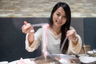 Restoran masasında güveç yiyen genç bir kadın.