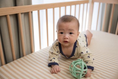 Bebek yuvarlanıyor ve yatakta top oynuyor.