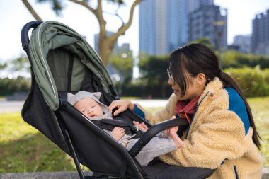 Kadın dışarıda bebek arabasında bebeğe bakıyor.