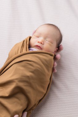 Yeni doğmuş bebek kahverengi kundak battaniyesinde uyuyor.