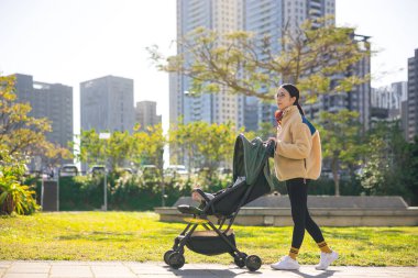 Bebek arabasıyla parkta yürüyen bir kadın.