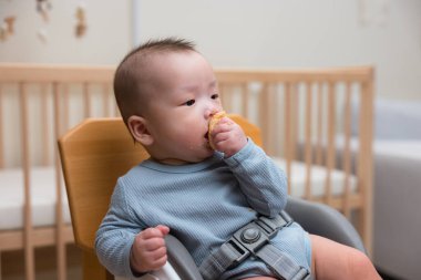 Bebek sandalyede oturmuş atıştırıyor.