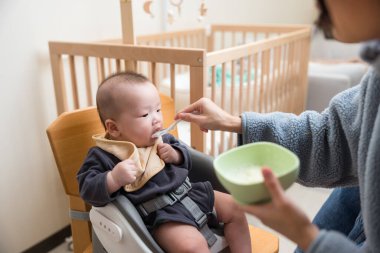 Anne kaşıkla beslenirken bebek katı yiyecekler yiyor.