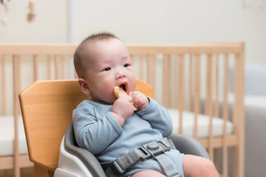 Küçük bebek yemek sandalyesinde oturmuş yemek yiyor.