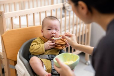 Anne bebeği kaşıkla katı besinle besliyor.
