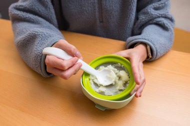 Eller, bebek süzgeci kullanarak ezilmiş yemek hazırlıyor.