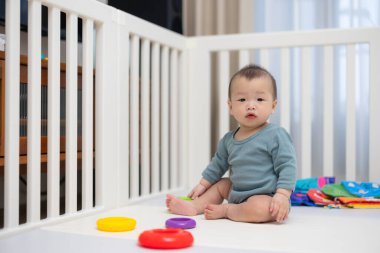 Evdeki beyaz oyun alanında oturan sevimli bebek.