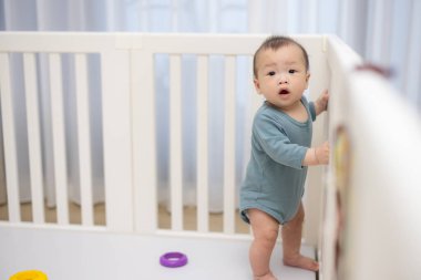 Bebek beşikte duruyor, tırabzanları tutuyor ve yukarı bakıyor.