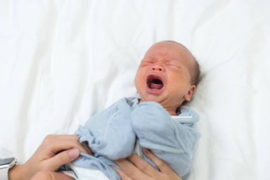 Anne yumuşak beyaz yatakta küçük bebeğe sarılıyor.