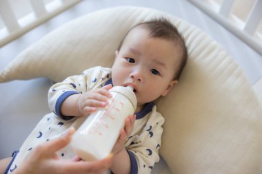 Bebek yastığa uzanmış süt içiyor.