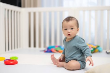 Çocuk parkında renkli oyuncaklarla oturan meraklı bebek.