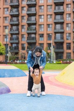 Anne, bebeğin parkta yürümesine yardım ediyor.