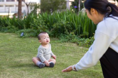 Anne, küçük oğluyla çayırda oynuyor.