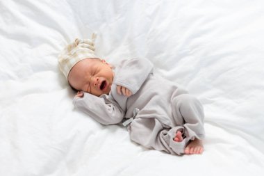 Şapkalı, ağlayan ve yatakta yatan Asyalı yeni doğmuş bebek.