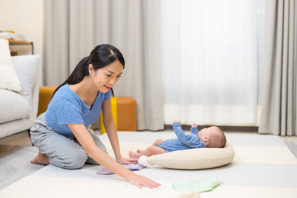 Mother cleaning playpen while baby watches at home