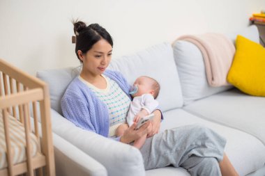 Annem kanepeye uzanmış bebeği tutarken telefonu kullanıyor.