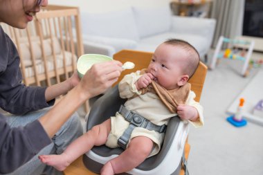 Anne ve baba, yüksek sandalyede oturan bebeği besliyor.