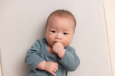 Tatlı bebek yumuşak elbiseler içinde elini emiyor.